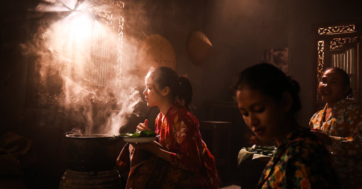 Women cooking traditional food in a warm, dimly lit kitchen with steam rising.