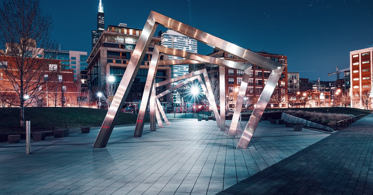 A sleek modern sculpture illuminated in an urban cityscape under a starry night sky.