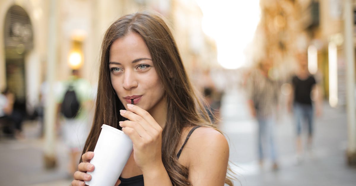 Woman sipping a beverage outdoors in a sunny city street, embodying leisure and enjoyment.