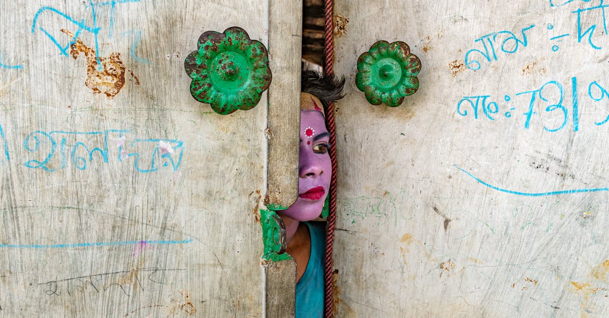 A person with vibrant face paint peeks through decorative doors with visible text.
