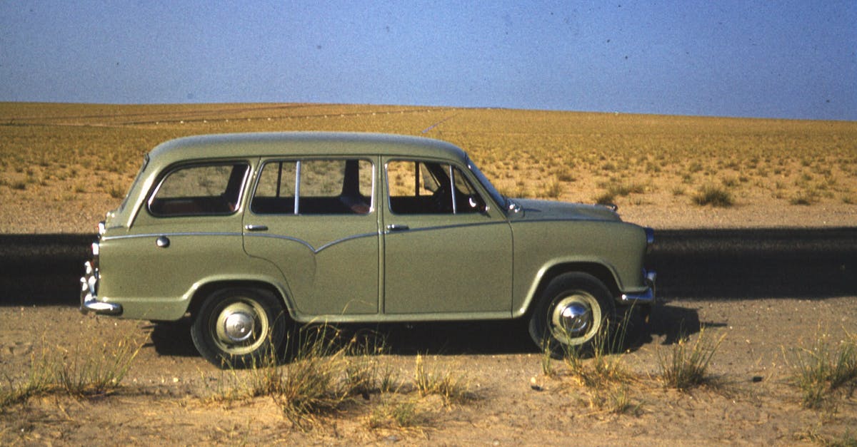 Classic Hindustan Ambassador car parked in a vast, arid desert landscape under a clear blue sky.