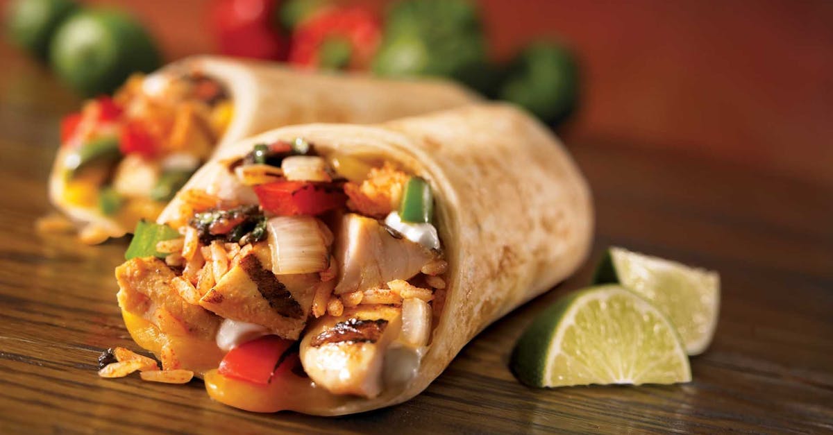 Close-up of a savory chicken burrito with fresh lime wedges, showcasing vibrant Mexican ingredients.