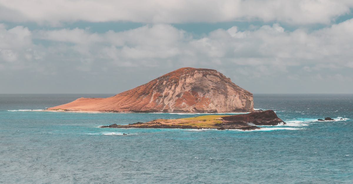 Stunning view of Mokoli'i Island surrounded by turquoise ocean under a partly cloudy sky.