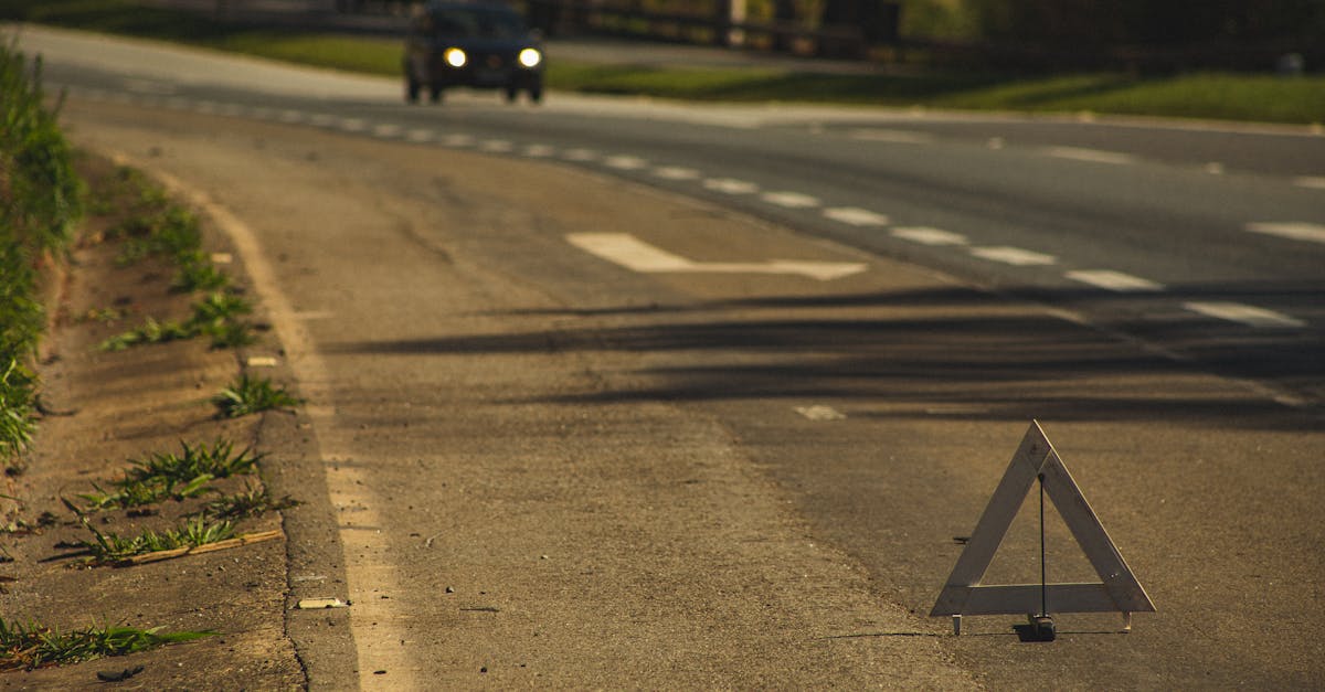 Automobile with headlights on driving on asphalt road with triangular sign in twilight