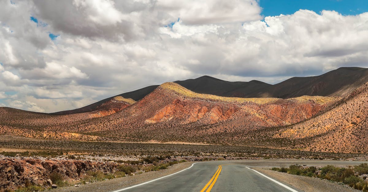 Wide highway cutting through remote desert landscape with mountains and cloudy sky.