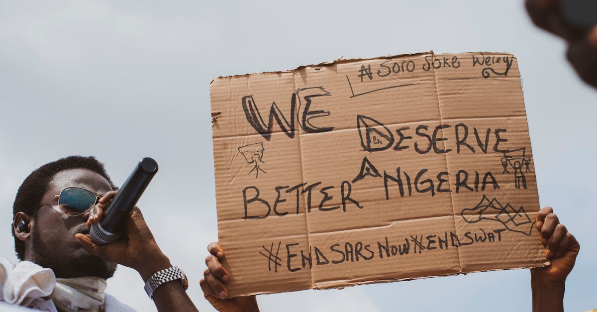A Nigerian protester speaks into a microphone while holding a cardboard sign demanding a better future.