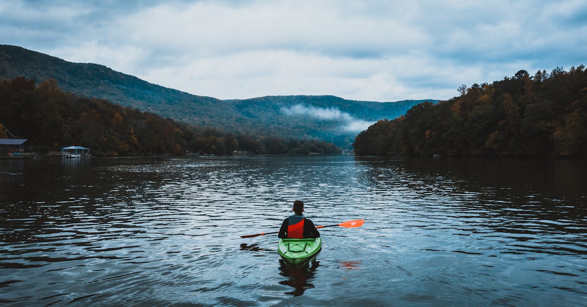 A lone kayaker paddles on a calm, misty lake surrounded by scenic mountains and autumn trees.