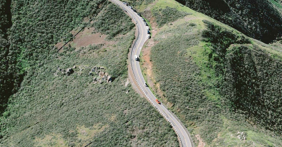 Drone view of curvy road going through countryside between green highlands on summer sunny day