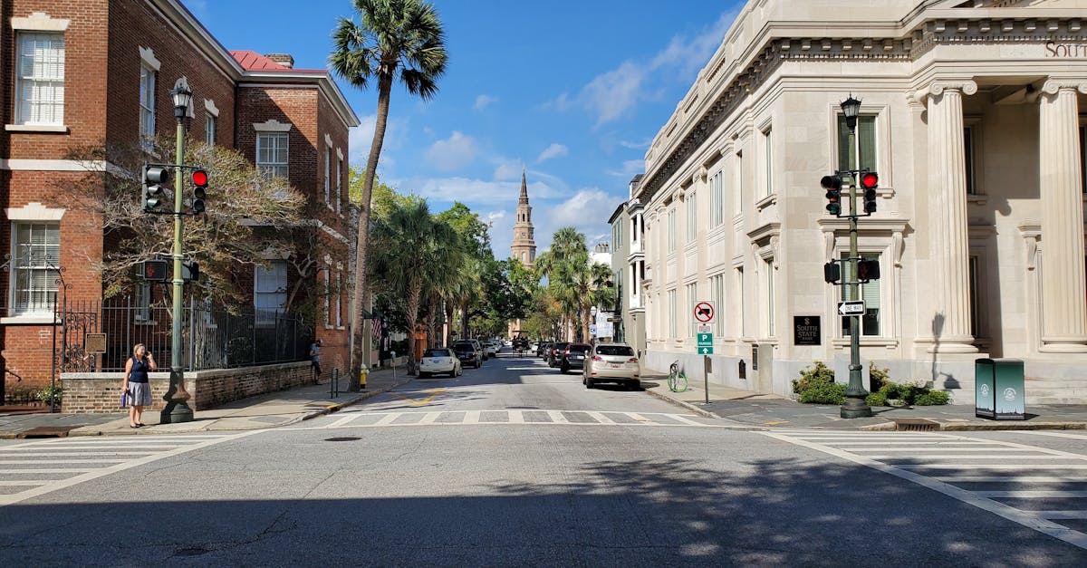 View of a sunny street with historic buildings, palm trees, and a church spire in the distance.