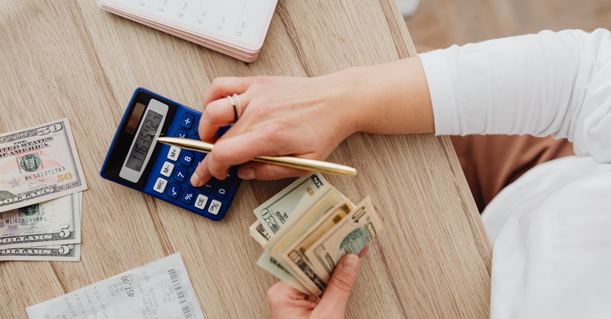 Person using a calculator and counting cash on a wooden table with receipts.