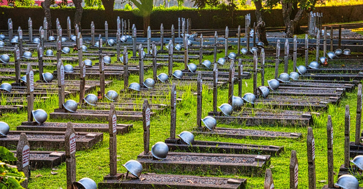 Tombstones with military hardhats located on grassy ground near tall green tall trees in national main heroes cemetery in Indonesia