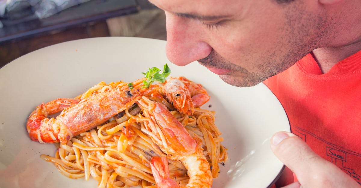 A man enjoys the aroma of a shrimp pasta dish with herbs. Perfect for food lovers.