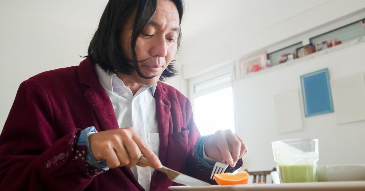 Asian man in a cozy home setting enjoying a healthy breakfast with fruits and a green smoothie.