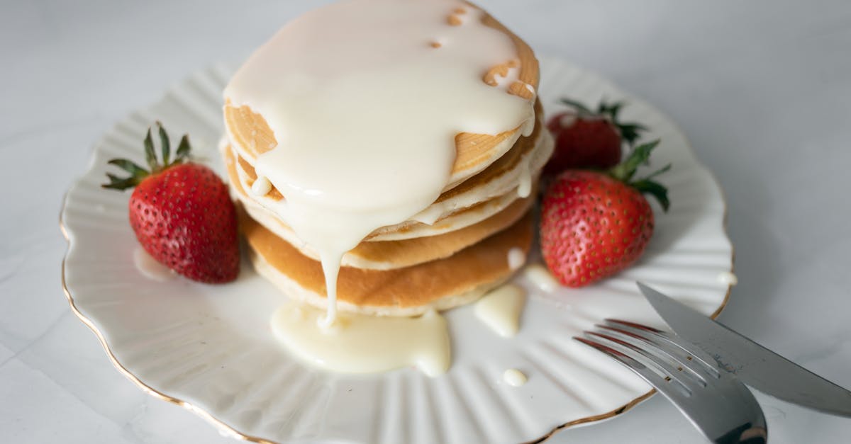 Delicious pancakes topped with cream and fresh strawberries on a plate.