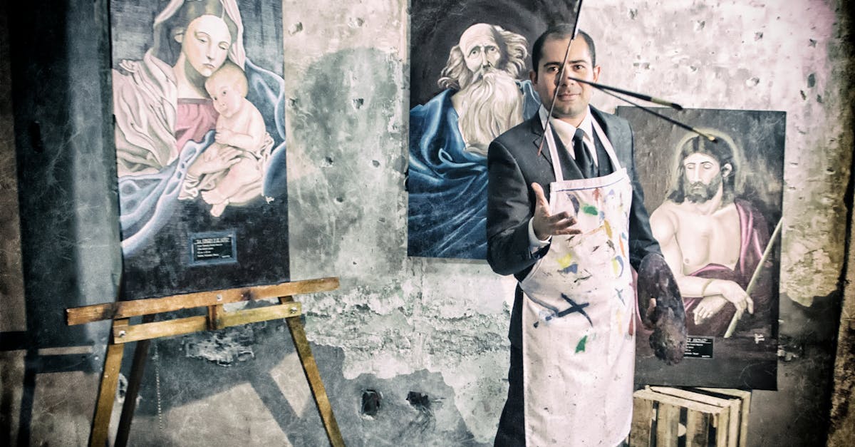 Artist in a suit and apron poses with Renaissance-style paintings in an old studio.