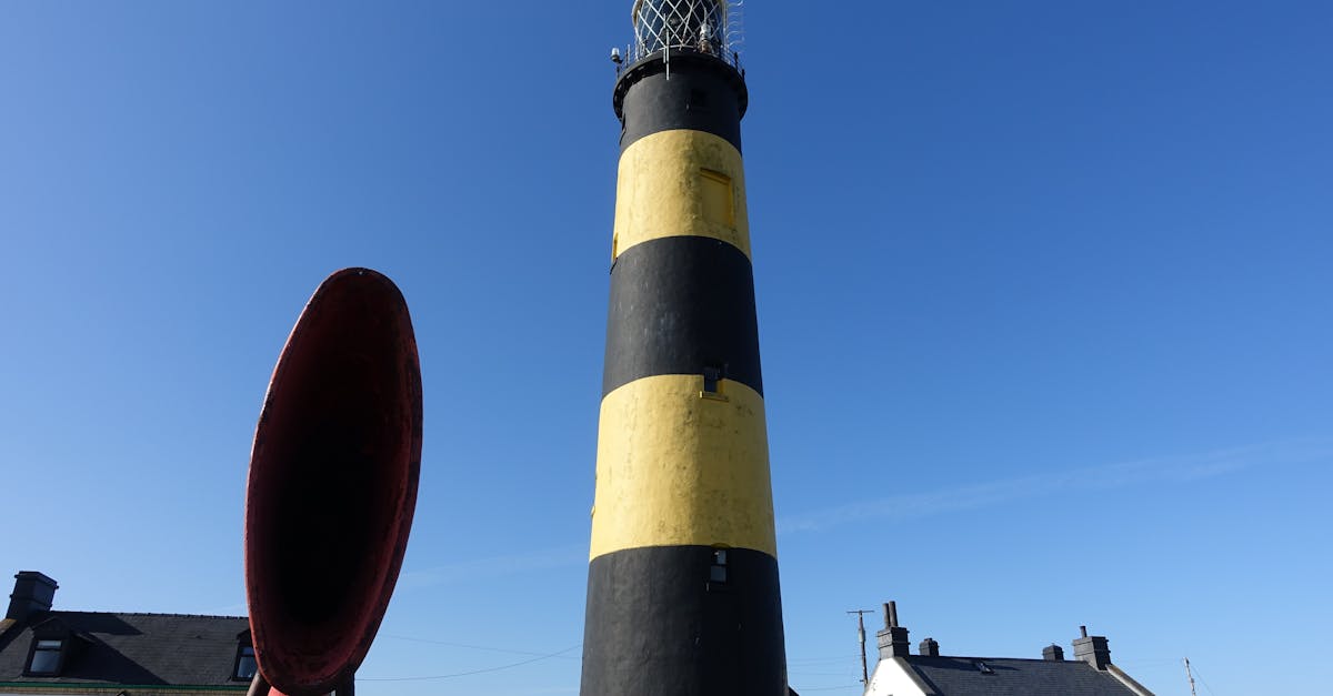 A bold black and yellow lighthouse stands tall under a clear blue sky, offering guidance.