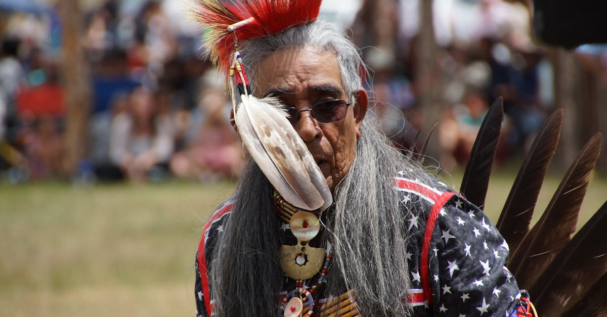 Senior Native American man in elaborate headdress and attire at a cultural gathering.