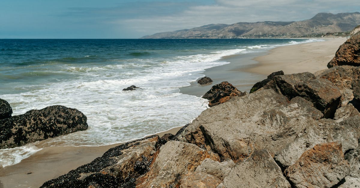 Beautiful rocky coastline with waves crashing against the shore under a bright blue sky.