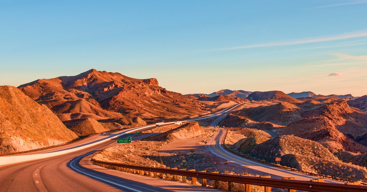 Stunning view of a winding highway amidst Nevada's rugged landscape under blue skies at sunset.