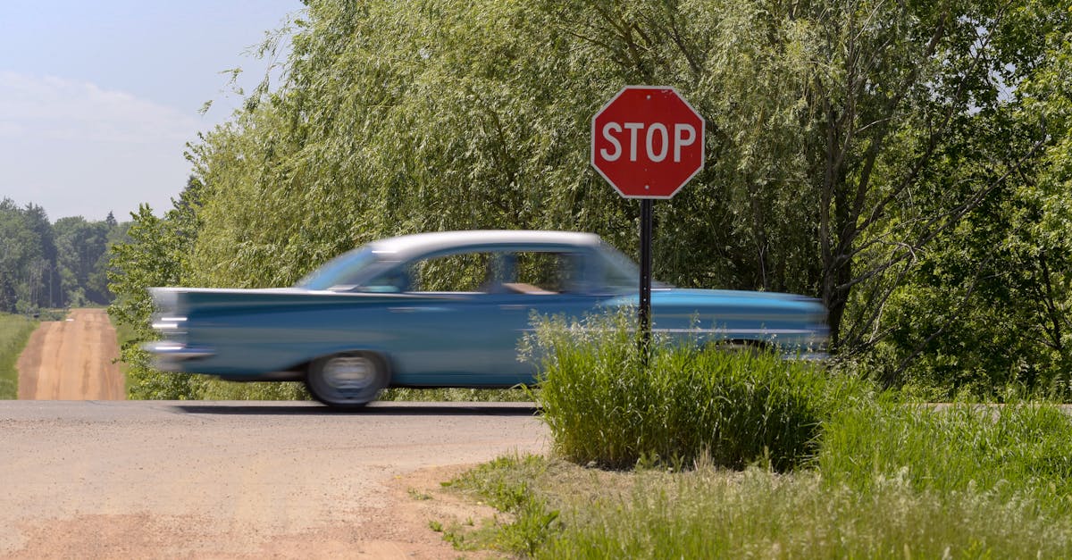 A classic blue car speeding past a stop sign on a rural dirt road.