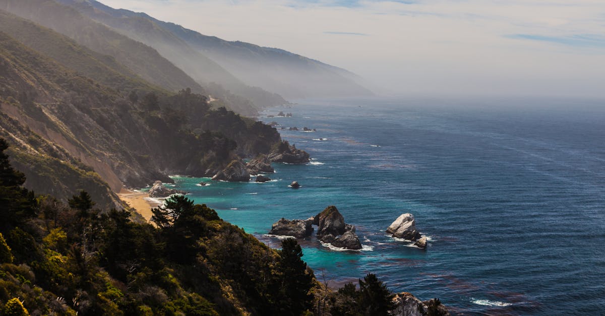 Explore the breathtaking landscape of rugged cliffs and clear blue ocean in this fog-kissed coastal scene.