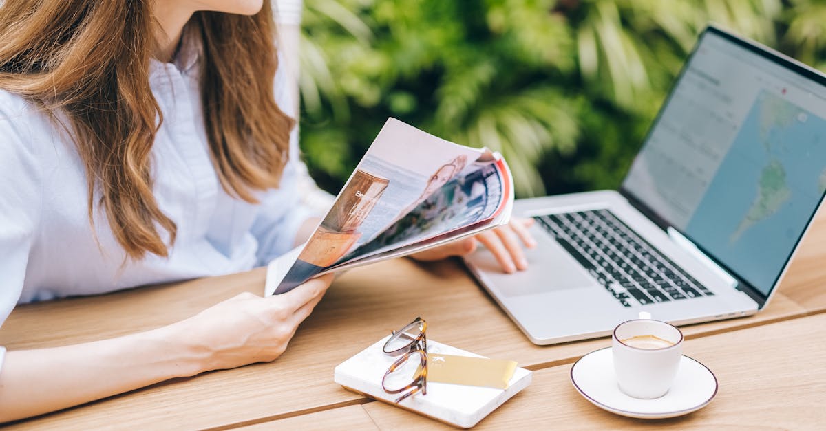 A woman sits outdoors, enjoying a magazine with coffee and laptop nearby.