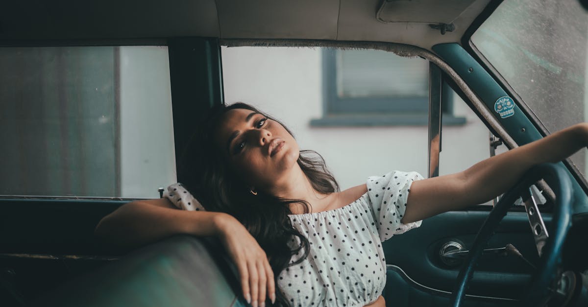 A young woman in a polka dot crop top relaxes inside a classic car, capturing a serene moment.